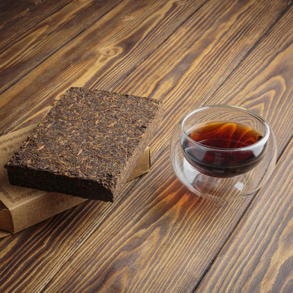 Puer tea in glass cup with compressed pu-erh on wooden background